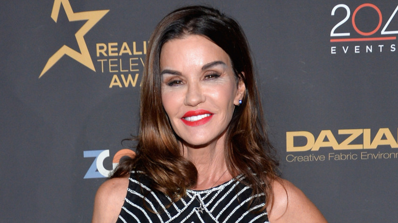 Janice Dickinson smiling at a red carpet event with red lipstick