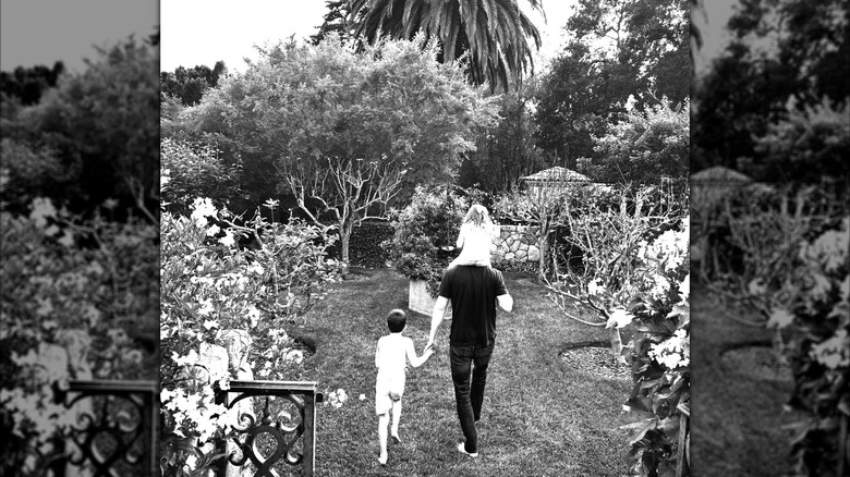 Prince Harry walking through a garden with Prince Archie and Princess Lilibet