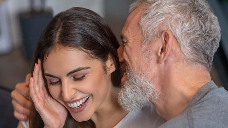 man whispering in smiling woman's ear