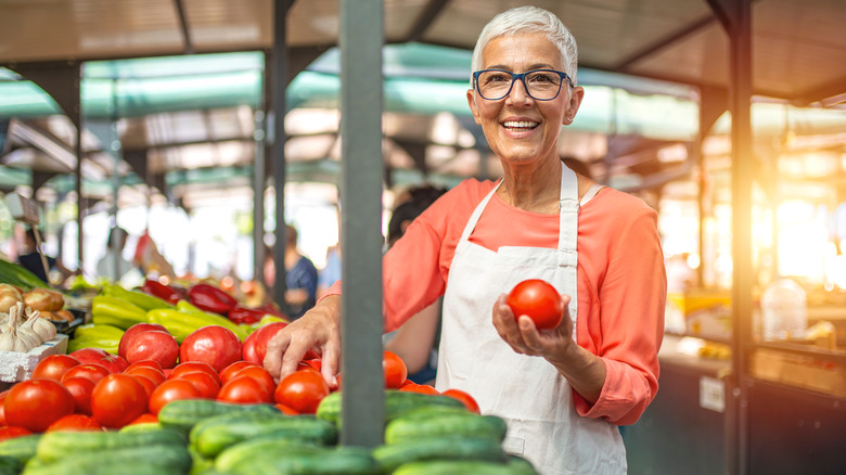 Woman smiling, holding a tomato among groceries