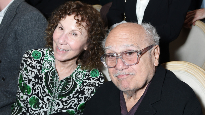 Rhea Perlman and Danny DeVito smiling while sitting together at an event