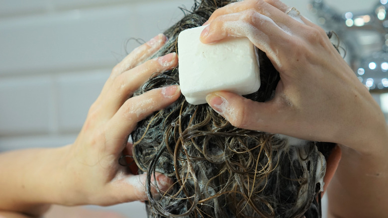 Brunette woman using a white shampoo bar to wash her hair.