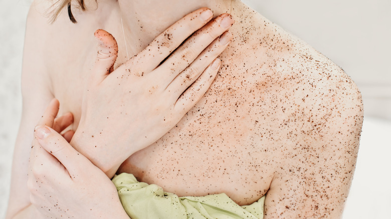 Woman in a towel rubbing a coffee scrub on her body