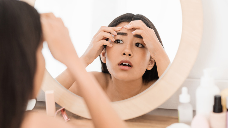 Young woman trying to pop a pimple while looking in the mirror 