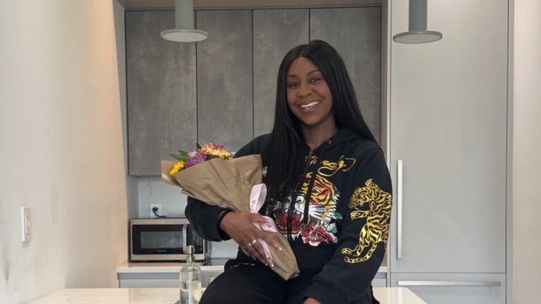 Ashley Smith wearing a hoodie with a tiger on it and holding a bouquet of flowers.