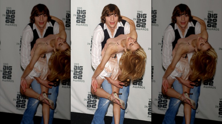 Ashton Kutcher wearing a striped shirt, black vest, and jeans holding Brittany Murphy as she's dipped backward in a peach dress