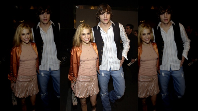 Brittany Murphy smiling in a peach dress with an orange jacket next to a surprised-looking Ashton Kutcher wearing a striped shirt, black vest, and jeans