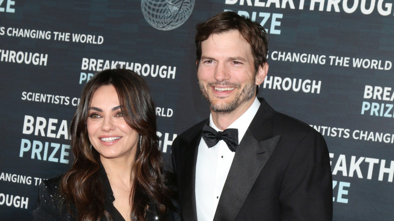 Ashton Kutcher and Mila Kunis smiling while posing together at a red-tie event