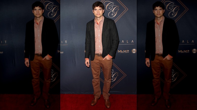 Ashton Kutcher posing in a pink shirt and gray blazer
