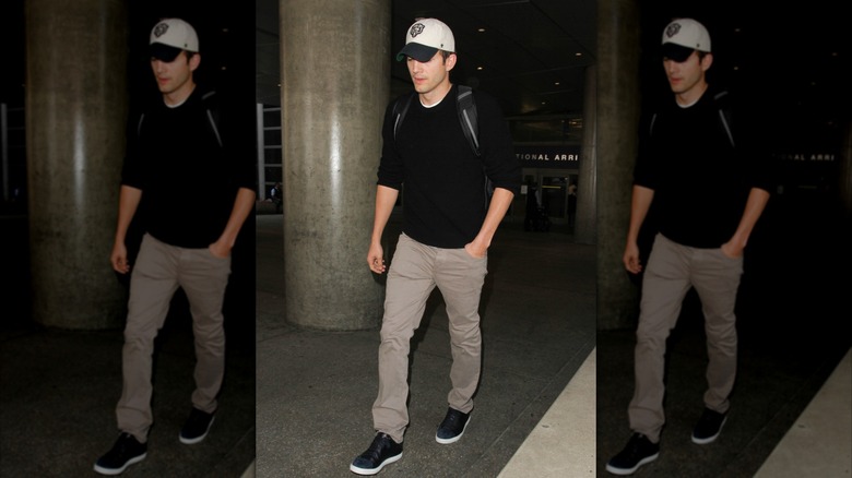 Ashton Kutcher walks with a black shirt and khaki pants