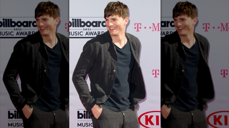 Ashton Kutcher smiling while posing in pin-striped pants and blazer