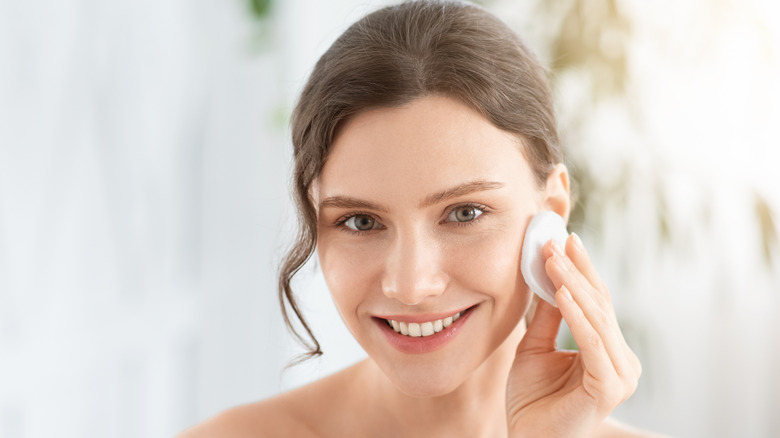 A smiling woman with a cotton pad on her face 