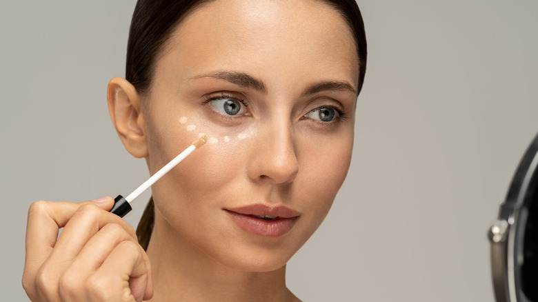 Woman applying concealer in mirror