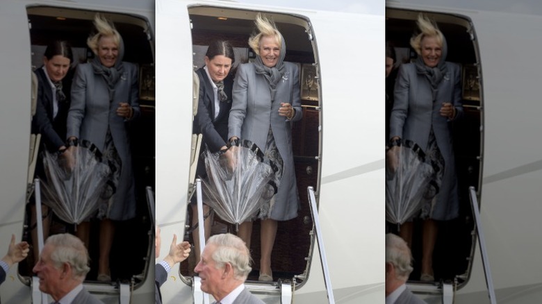 Camilla Parker Bowles struggling with an umbrella as she exits an airplane behind King Charles