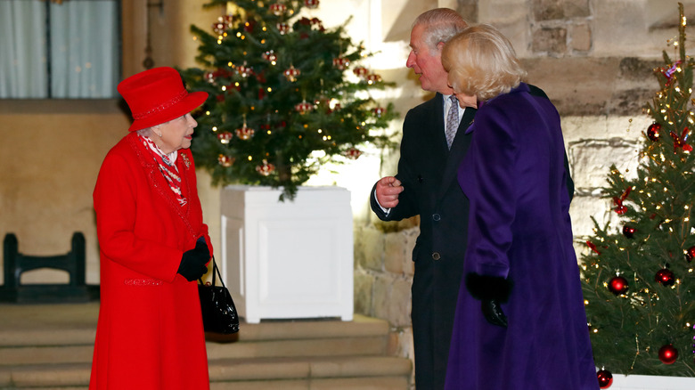 Queen Elizabeth talking to Prince Charles and Camilla outside surrounded by Christmas trees