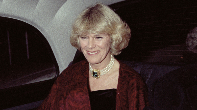 Camilla Parker-Bowles smiling in the back of a car in 1995 with red shawl draped over a black dress