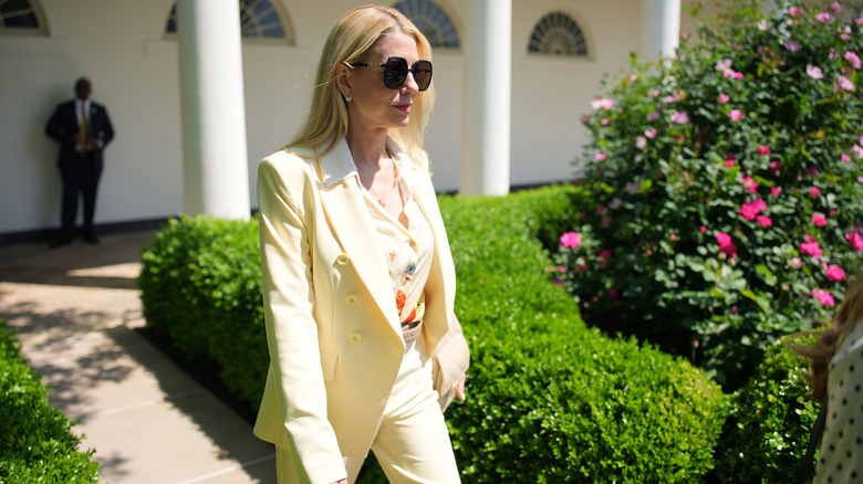 Pam Bondi walking while wearing a light yellow suit with sunglasses