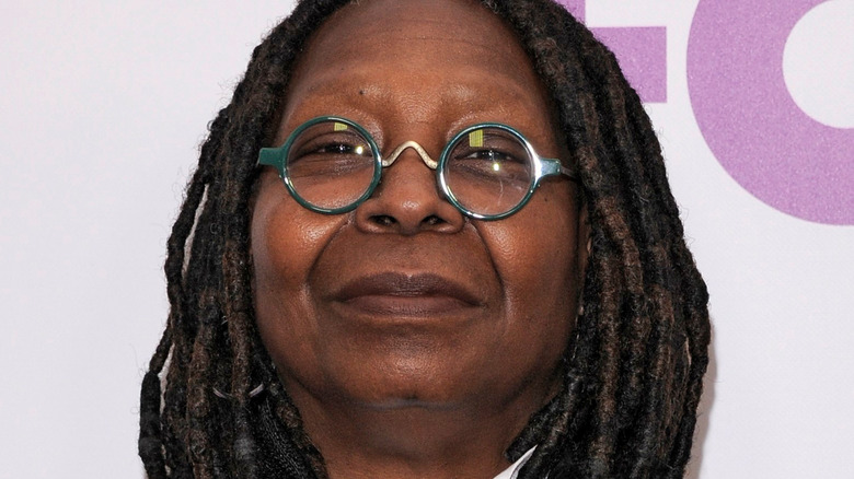 Whoopi Goldberg in green glasses holding mic