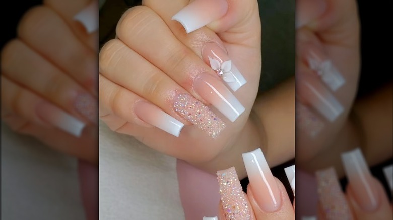 Close-up of pink and white ombre nails with rhinestones on the ring finger and a flower on the pointer finger