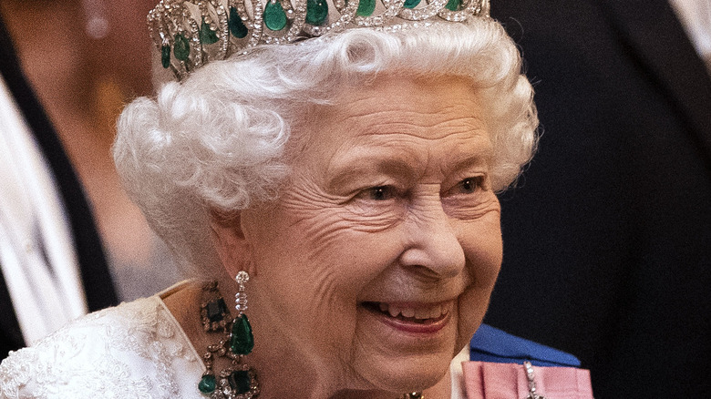 Queen Elizabeth wearing red hat and smiling