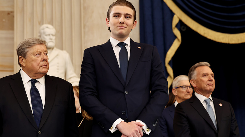 Barron Trump smiling in a navy suit with a matching tie