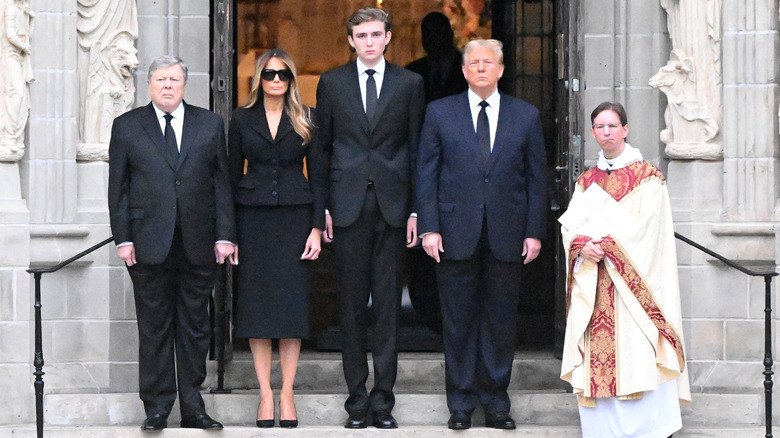 Viktor Knavs, Melania Trump, Barron Trump and Donald Trump standing outside on the steps of the church at the funeral of Amalija Knavs
