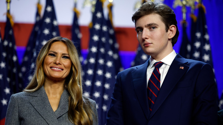 A smiling Melania Trump standing next to Barron Trump in a suit