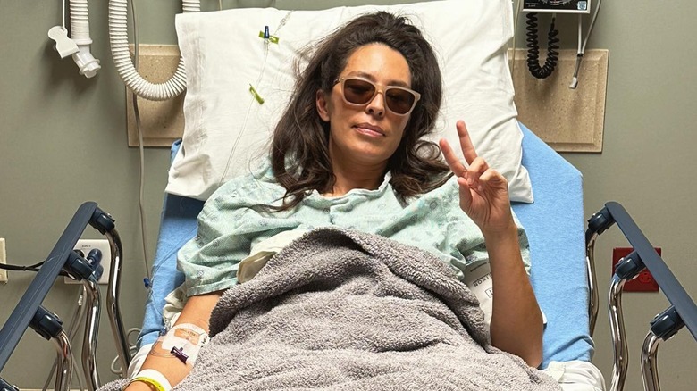 Joanna Gaines in a hospital bed making the peace sign