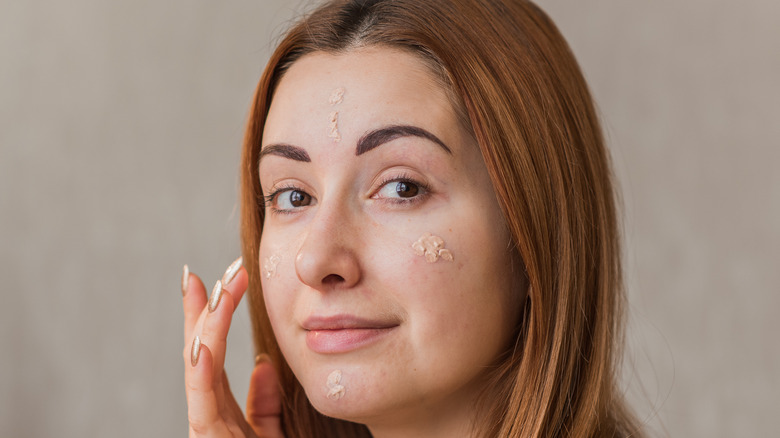 Woman applying concealer to her acne-prone skin.