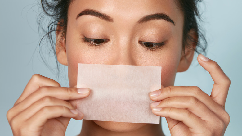 Brunette woman holding a blotting paper near her face.