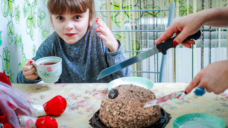 Young girl with mom cutting cake with a knife