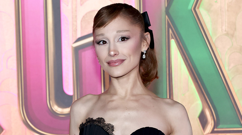Ariana Grande in a black dress with a black bow in her hair in front of Wicked sign