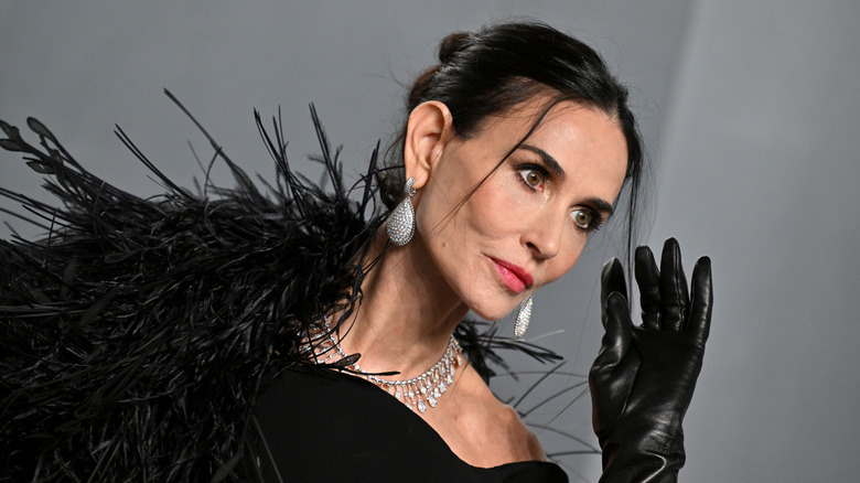Demi Moore wearing diamond jewelry, black leather gloves, and a black dress embellished with feathers.