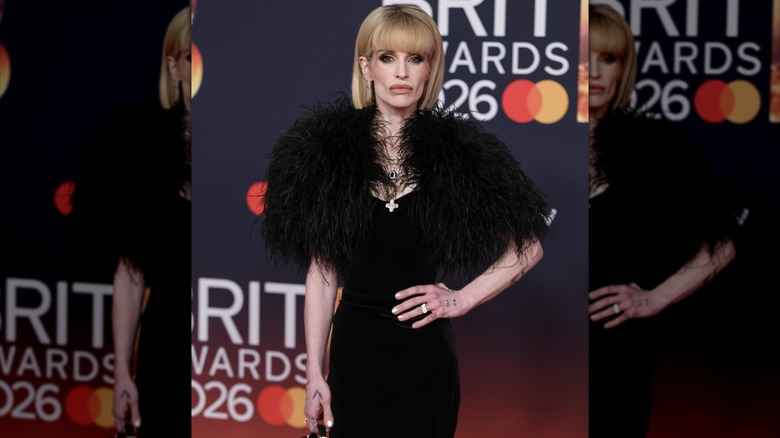 Kelly Osbourne posing with a hand on her hip in a black dress and feathered shrug.