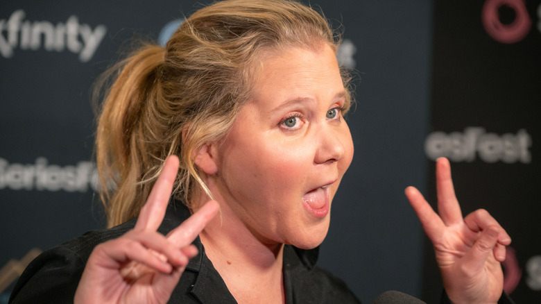 image of Amy Schumer looking happy at an event with both hands making the "peace" sign