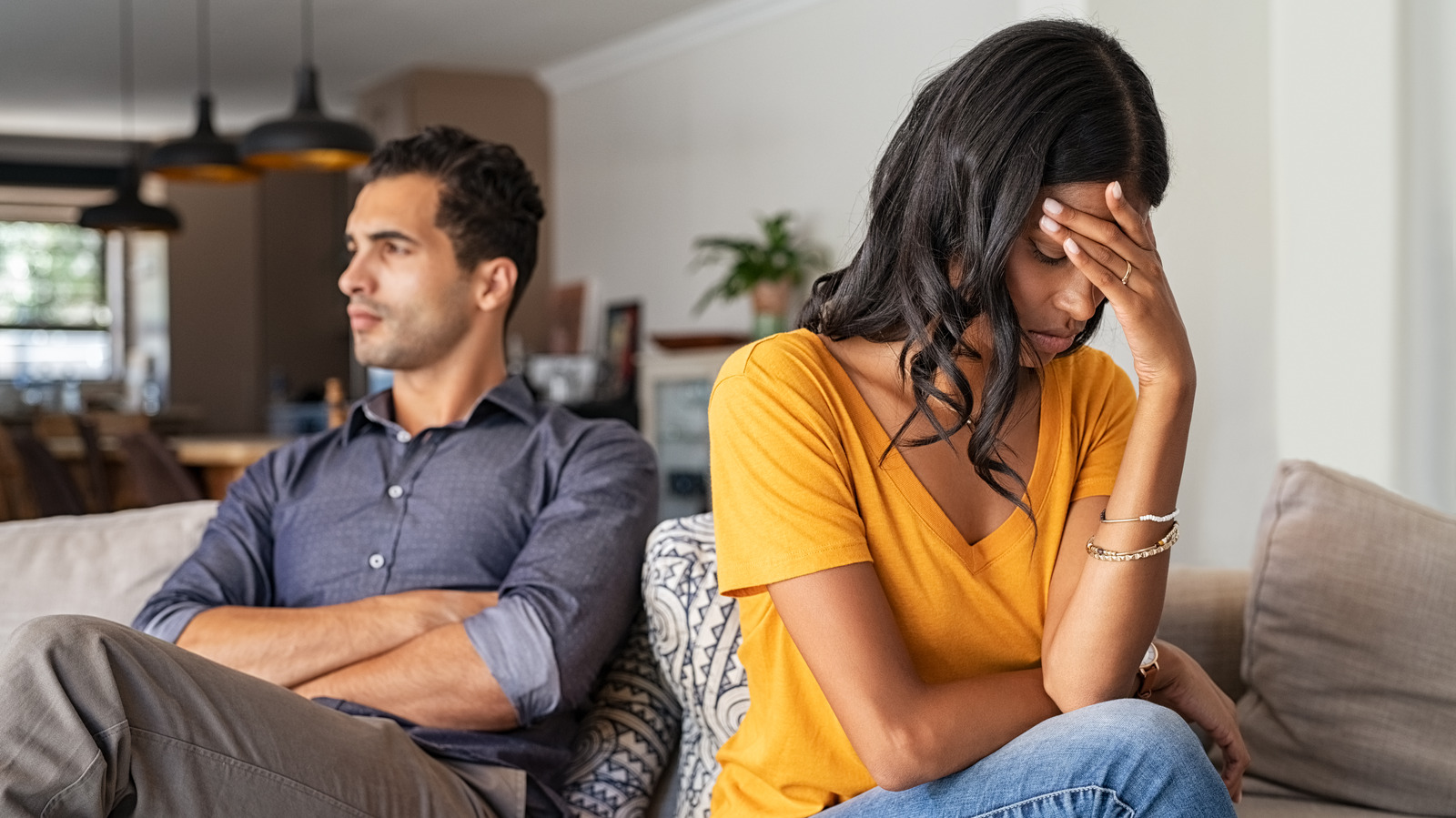 Couple sitting apart on a couch, showing emotional distress, reflecting relationship issues related to legal consequences and personal struggles.