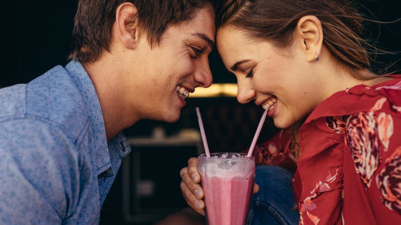 Man and woman on date sharing strawberry milkshake