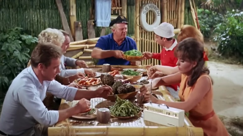 The cast of Gilligan's Island eating a feast in front of the shack on the island, on an episode of Gilligan's Island