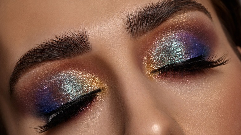 Close-up of woman's eyes wearing colorful metallic cream shadow look