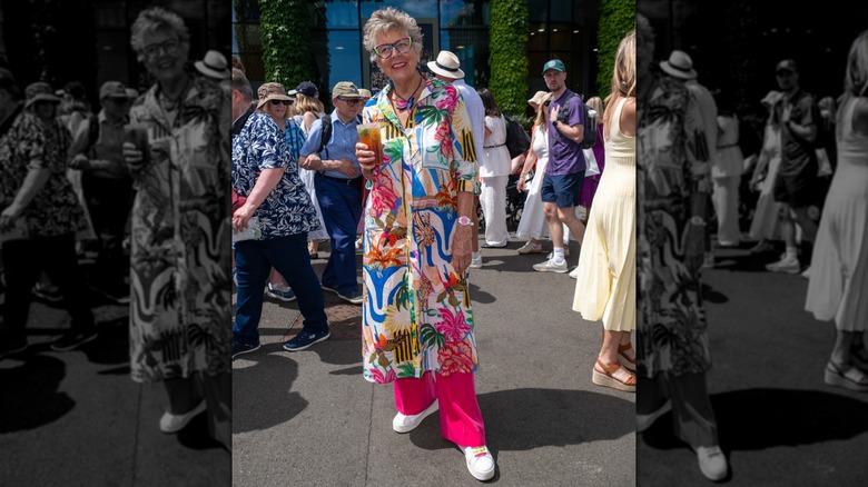 Prue Leith in a brightly colored outfit and holding a glass of Pimm's at Wimbledon.