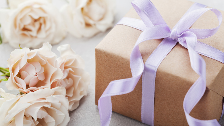 White flowers and a tan gift box tied with purple ribbon