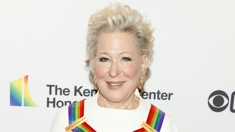 Bette Midler smiling while wearing a rainbow piece