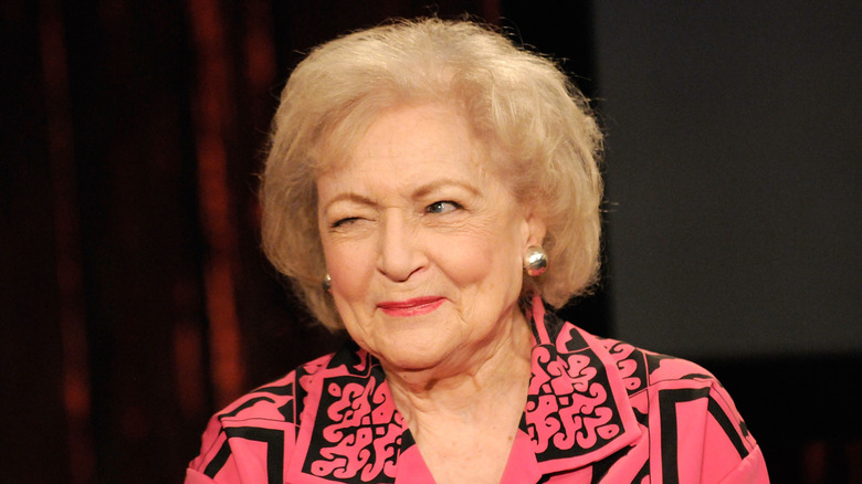 Betty White in a pink and black patterned shirt, giving a wink to someone off camera