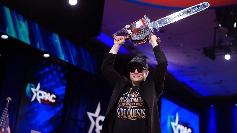 Elon Musk holding a chainsaw over his head
