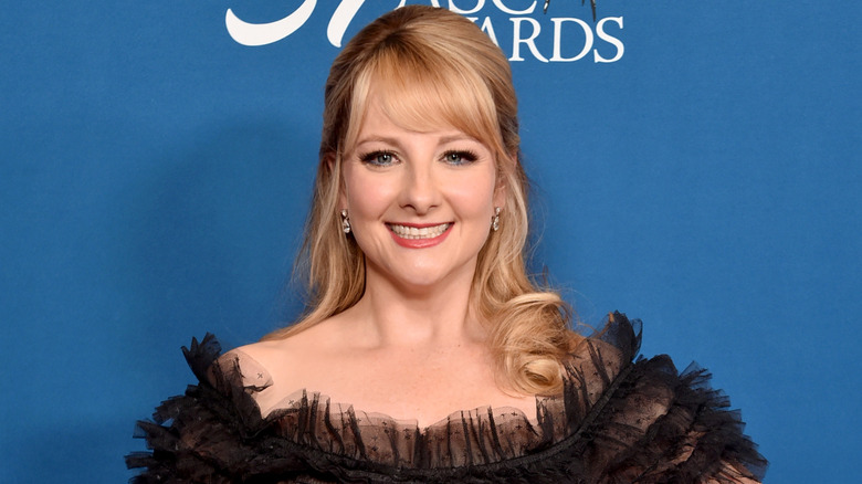 Melissa Rauch smiling while posing at an event in a ruffled black dress