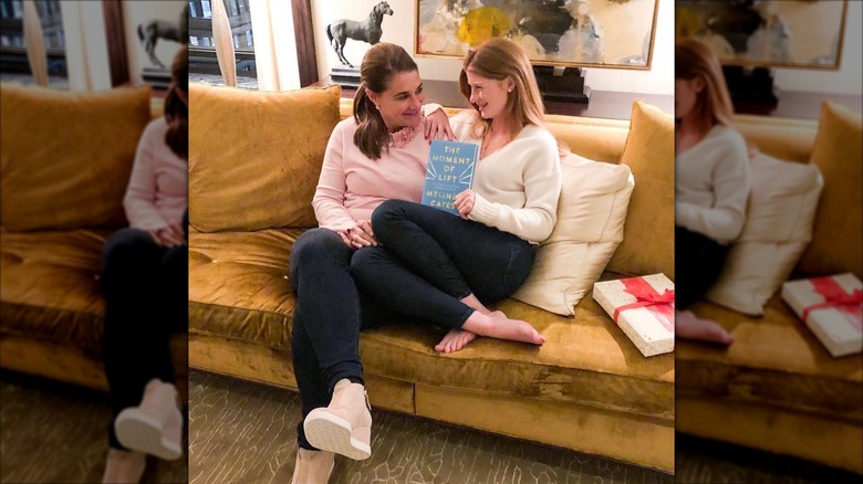 Jenn and Melinda Gates smiling at each other on a couch holding Melinda's book "The Moment of Life"