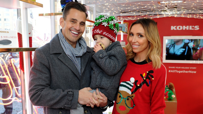 Bill Rancic and Giuliana Rancic smiling and holding their son while posing together at Christmastime