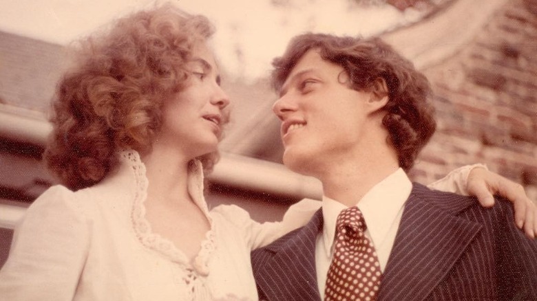 Hillary Clinton in a white dress and Bill Clinton in a suit outside