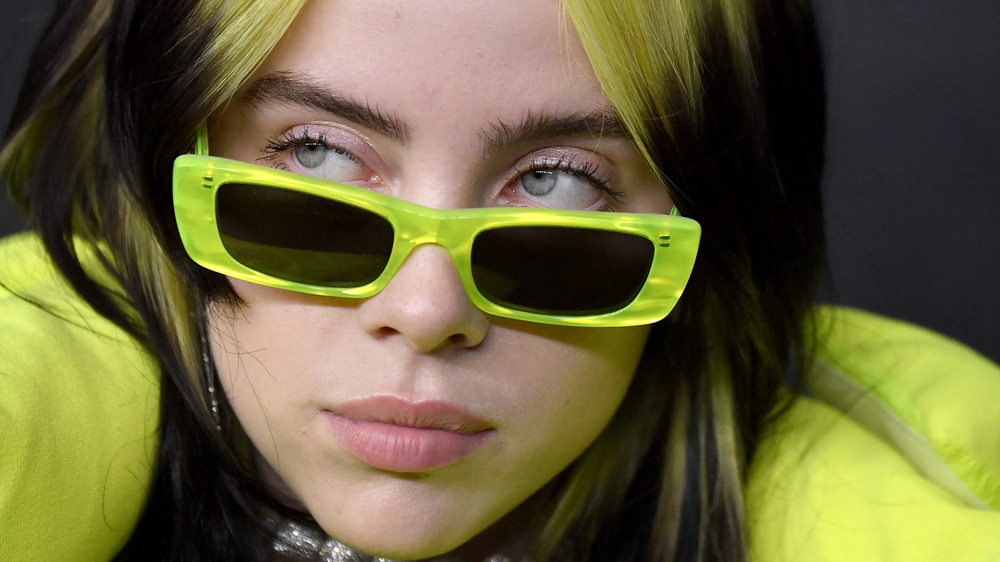 Billie Eilish looking serious with neon green hair and glasses