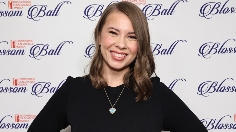 Bindi Irwin midlength bob, nude lip, blue heart necklace, black top